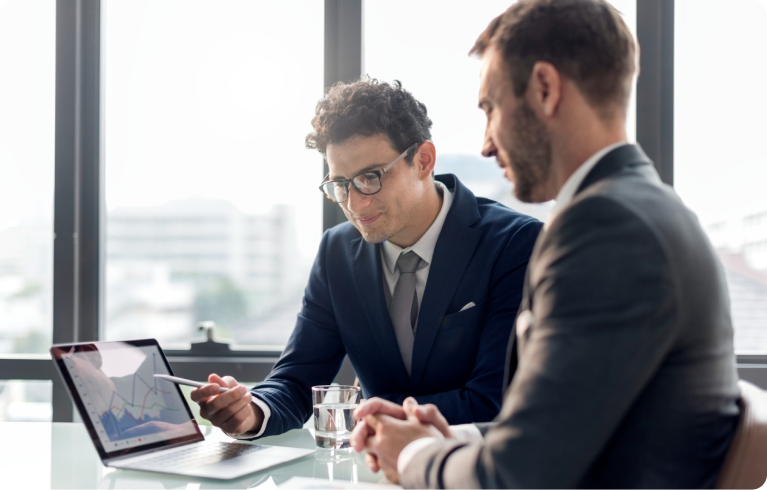 Two men engaged in a discussion about business charts displayed on a laptop, analyzing data and strategies for small business consulting